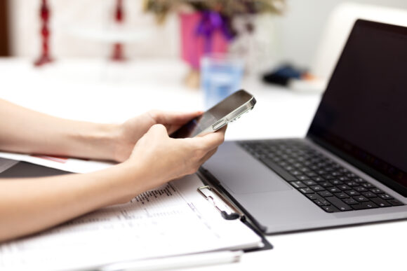 A woman looking at her phone and laptop trying to access an account.